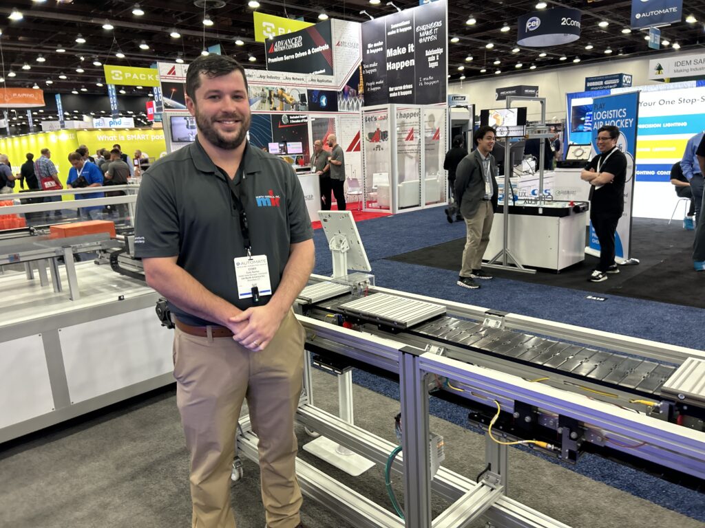 Cory Santor, inside sales manager for mk North America, stands next to the company’s SPU 2040, a recirculating pallet system that utilizes pneumatic stops to transport goods.