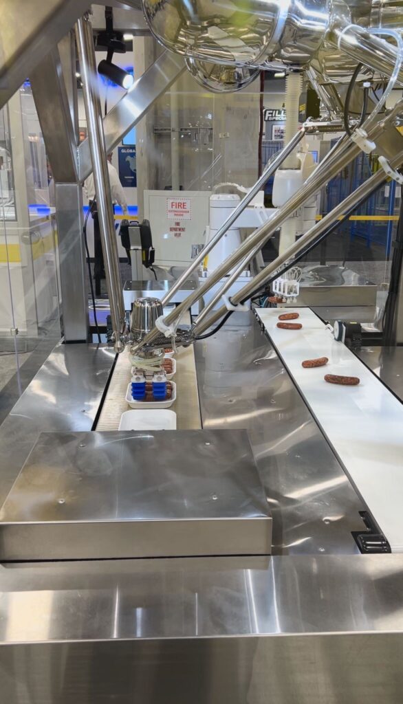 Fanuc demonstrated Delta and SCARA robots for primary packaging at Pack Expo 2025 at the Las Vegas Convention Center, including a cell packing sausage products. The photo shows the DR-3iB/6 Stainless IP69K-rated delta robot and a food-grade SR-12iA/C SCARA robot placing sausage links in packages. The system meets USDA and FDA sanitation standards using vacuum grippers and Fanuc’s iRPickTool for placement in washdown environments.
