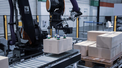 Industrial robot arm loading cartons on a conveyor, highlighting warehouse and end-of-line packaging automation, robotics, and automated case packing solutions.