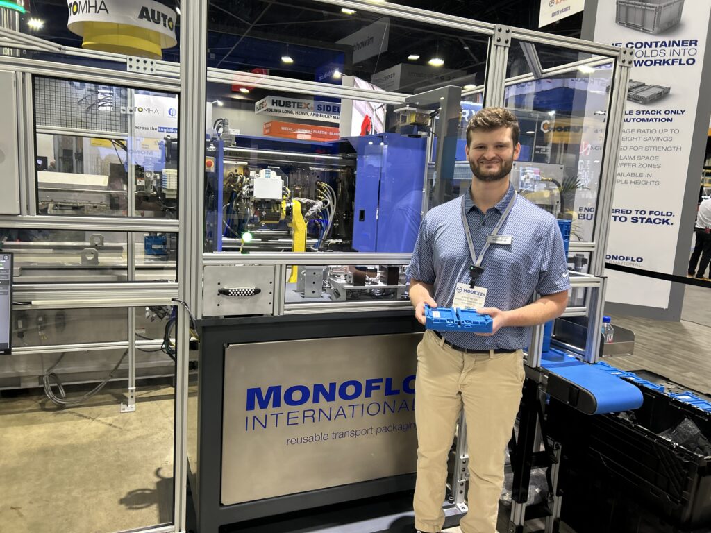 Josh Meyer, production manager at Monoflo, at Modex 2026 in Atlanta, Georgia, standing next to a live production demo of the company’s foldable FSO containers. The system features injection molding, robotic part handling and label placement, vision-based quality inspection, and automated sorting of accepted and recheck parts.
