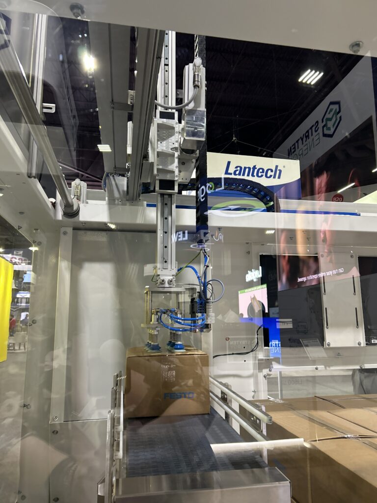 The CODI Flex Stack, a compact gantry-style palletizer built with Festo controls, shown in operation at Modex 2026 in Atlanta, Georgia, moving Festo-branded boxes.