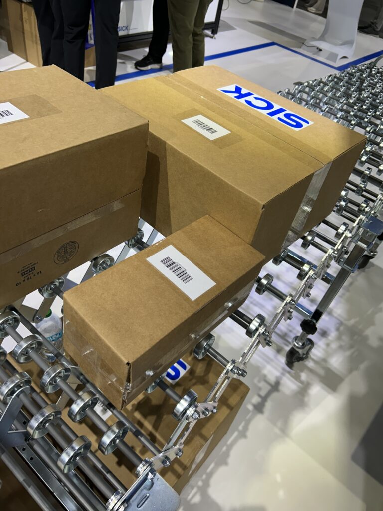 Cartons staged on a conveyor at Modex 2026 in Atlanta, Georgia, as part of SICK’s vision-based manifest verification system for automated barcode reading.