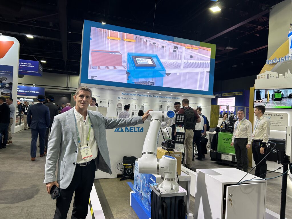 Bill Faber, Director of Product Marketing and Business Development, Industrials Segment at Delta Electronics Americas, at Modex 2026 in Atlanta, Georgia, standing in front of the company’s booth showcasing its automation technologies, including a collaborative robot (cobot).