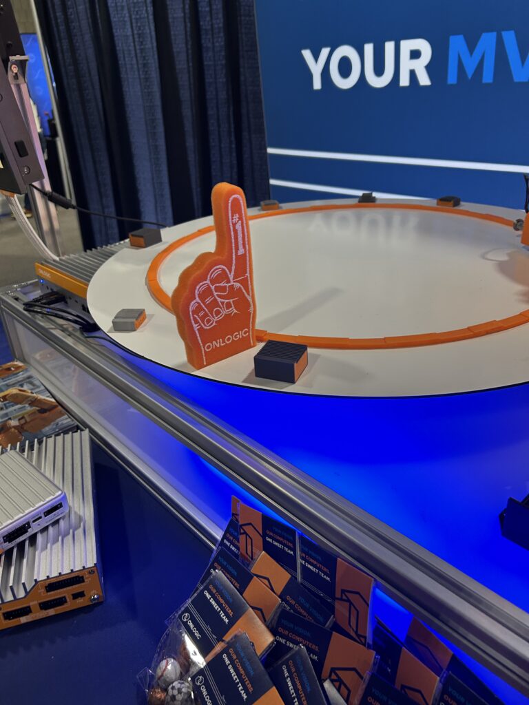 An OnLogic foam finger displayed on a machine vision demo at Modex 2026 in Atlanta, Georgia, powered by the company’s industrial PCs for edge computing applications. The booth carried a sports theme, with the company noting that sports is a unifying concept across industries.
