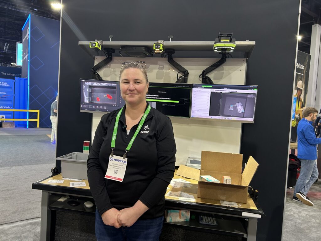 Samantha Frost, program manager advisor at Zebra Technologies, stands in front of the company’s Packing Bench demo. The system uses RFID and fixed industrial vision systems to verify barcodes and text, including lot codes and expiration dates.