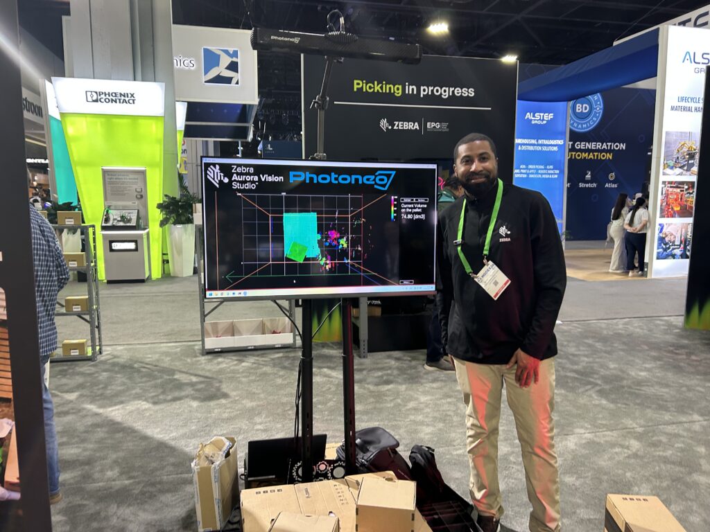 Ken Williams at Zebra Technologies stands next to the Foxy Scanner Gen 3 at Modex 2026 in Atlanta, Georgia, using a blue laser to capture 3D point cloud data of a pallet for dimensioning applications.