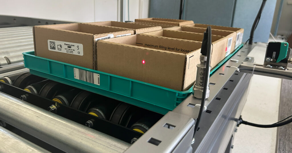 Pepperl+Fuchs industrial sensor lab demonstrates conveyor automation with a photoelectric sensor detecting tote movement for zone-based material handling and packaging efficiency.