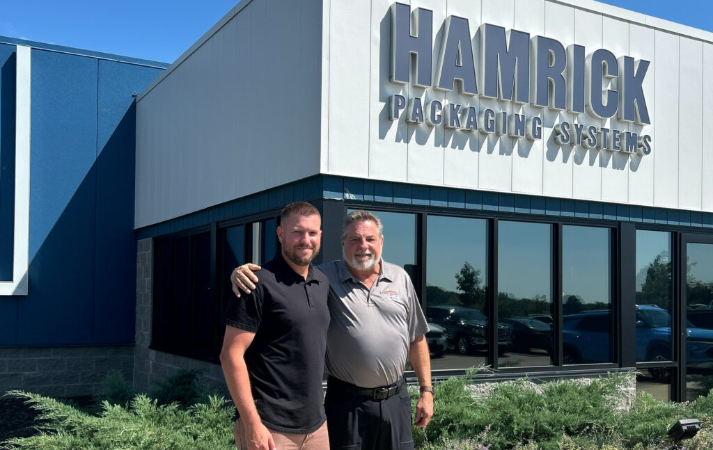 Jordan Hamrick and Phil Hamrick stand outside Hamrick Packaging Systems’ facility in Kent, Ohio. On May 1, the OEM announced a leadership transition with Jordan Hamrick named President and CEO, succeeding his father, Phil, who will move to chairman of the board after decades leading the company. Photo taken by Packaging OEM during an August 2025 visit.