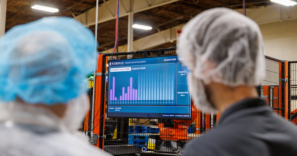 Attendees at a Formic event viewing a production intelligence dashboard tracking Wyandot Snacks palletizer performance, including cases per hour, uptime, and throughput data across the end-of-line system