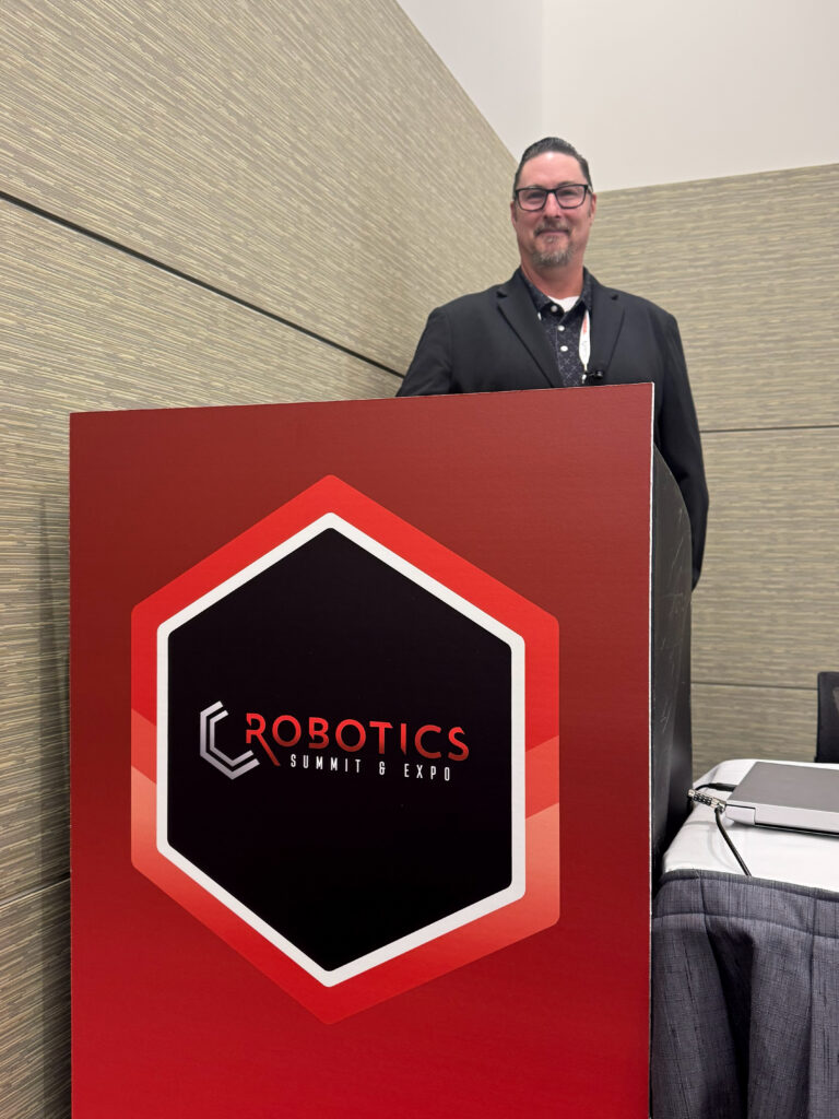 Chris Morgan, senior director of R&D at Bastian Solutions, poses at the podium after presenting "Where AI Delivers in Material Handling" at the 2026 Robotics Summit & Expo in Boston.
