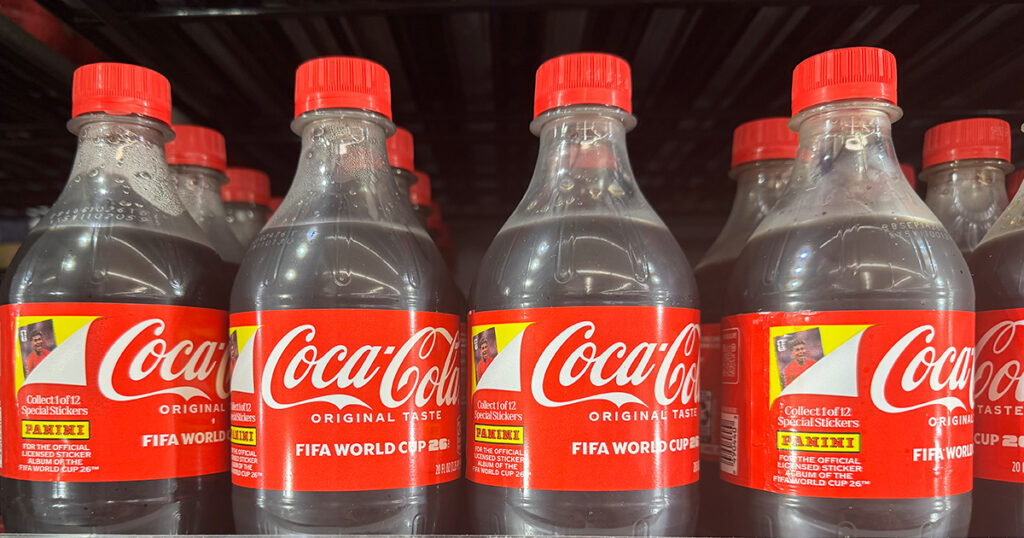 Coca-Cola bottles with Panini collectible labels are displayed on an Ohio retail shelf, showcasing the brand’s FIFA World Cup packaging campaign.