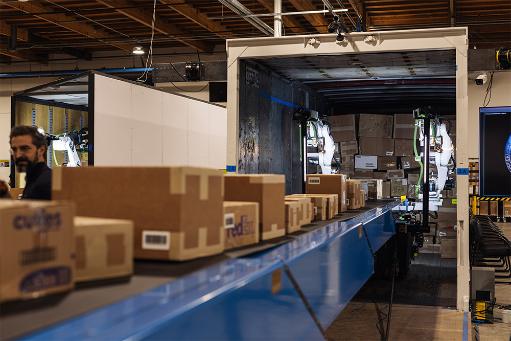 Packages move along a conveyor toward the Mech for automated truck loading.