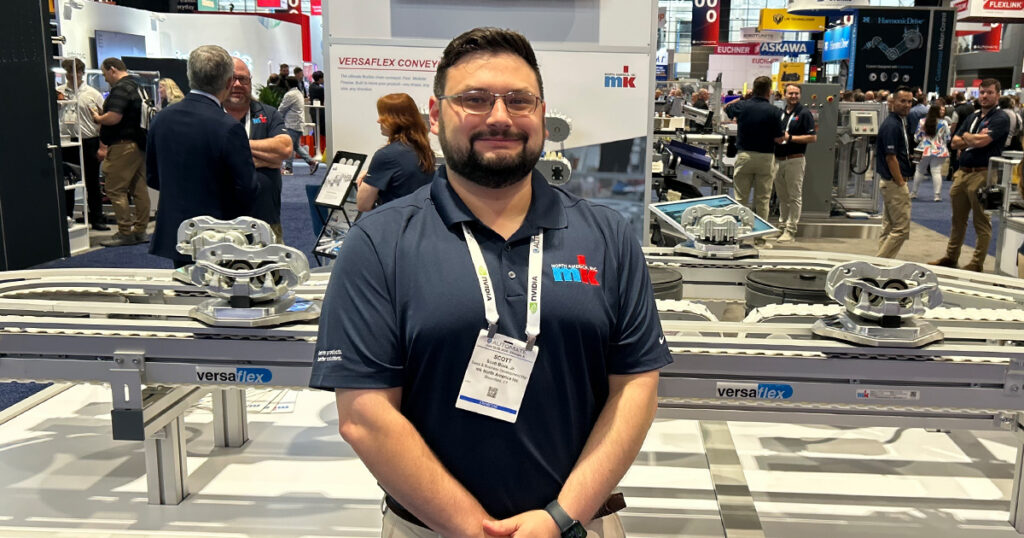mk North America sales and business development manager Scott Blais Jr. stands next to the VersaFlex conveyor at Automate 2026, which features a QR code for access to equipment information.