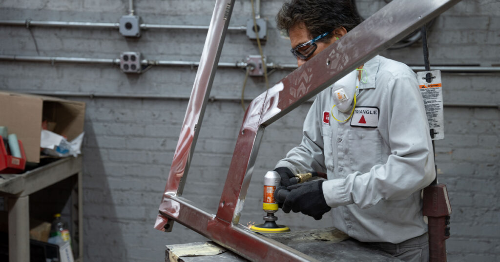A Triangle Package Machinery employee sands a metal frame on the shop floor.