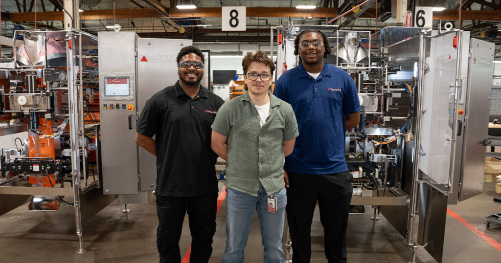 Triangle Package Machinery employees stand in front of assembly bays at the company’s Chicago manufacturing facility,