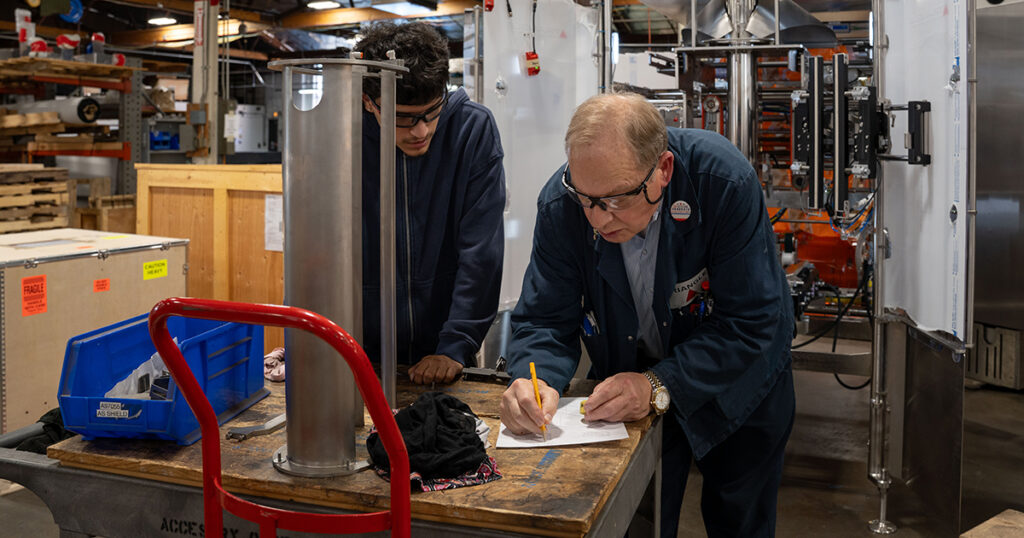 Triangle Package Machinery employees work together on the shop floor, sharing packaging machinery manufacturing knowledge and experience as the family-owned OEM prepares its next generation of workers.